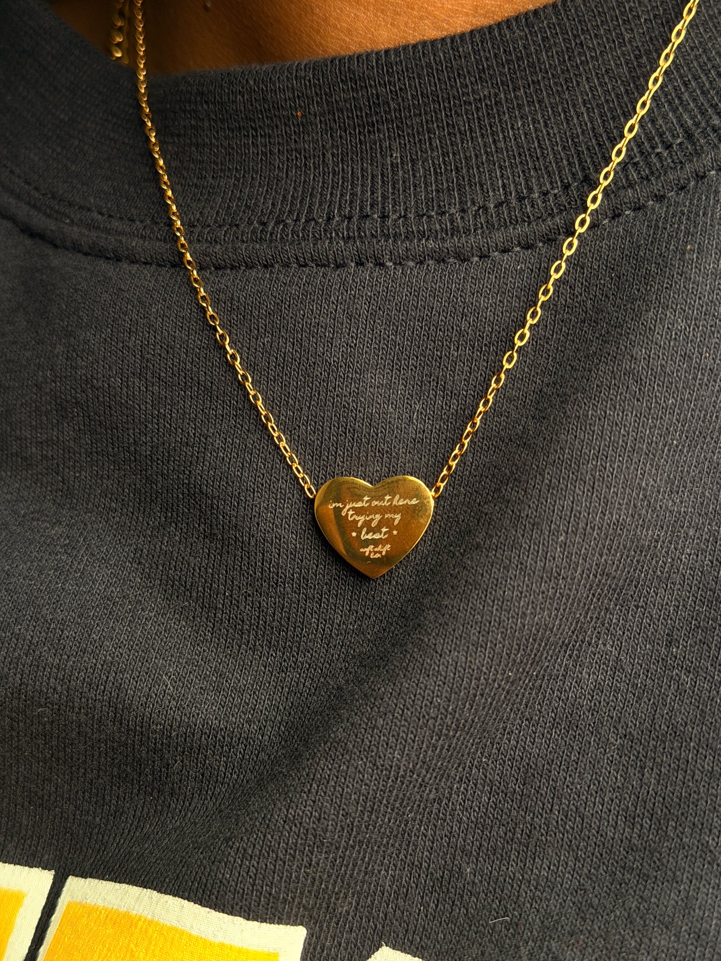 Gold heart-shaped pendant on a chain against a dark fabric background